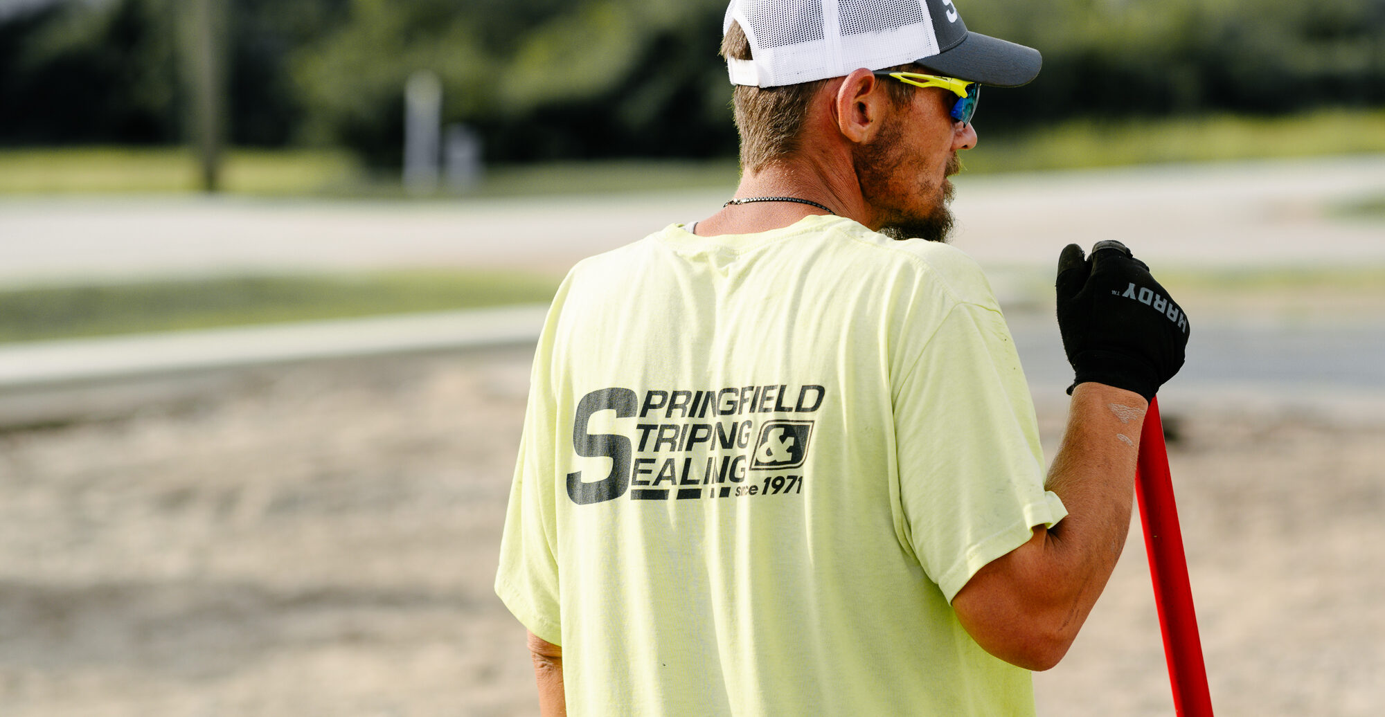 Worker in yellow shirt by Springfield Striping truck, broken asphalt.