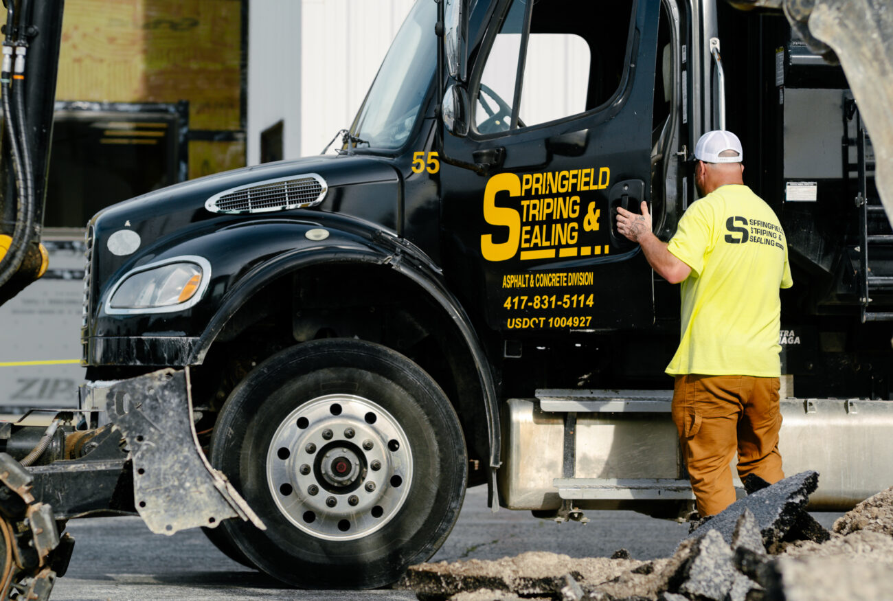 Worker in yellow shirt by Springfield Striping truck, broken asphalt.