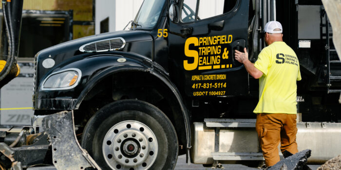 Worker in yellow shirt by Springfield Striping truck, broken asphalt.