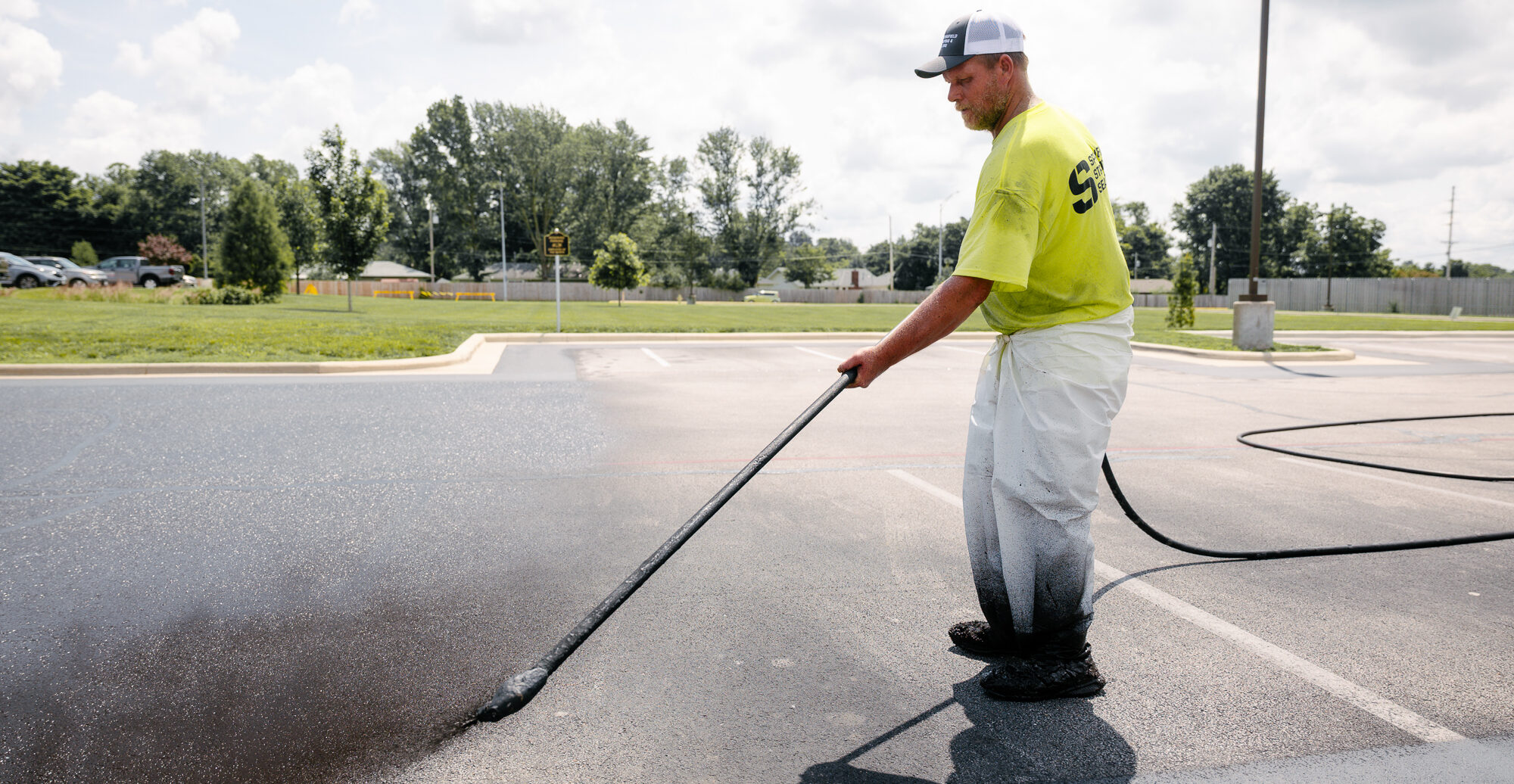 Worker sealing parking lot with long-handled sprayer.