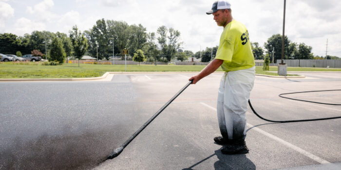 Worker sealing parking lot with long-handled sprayer.