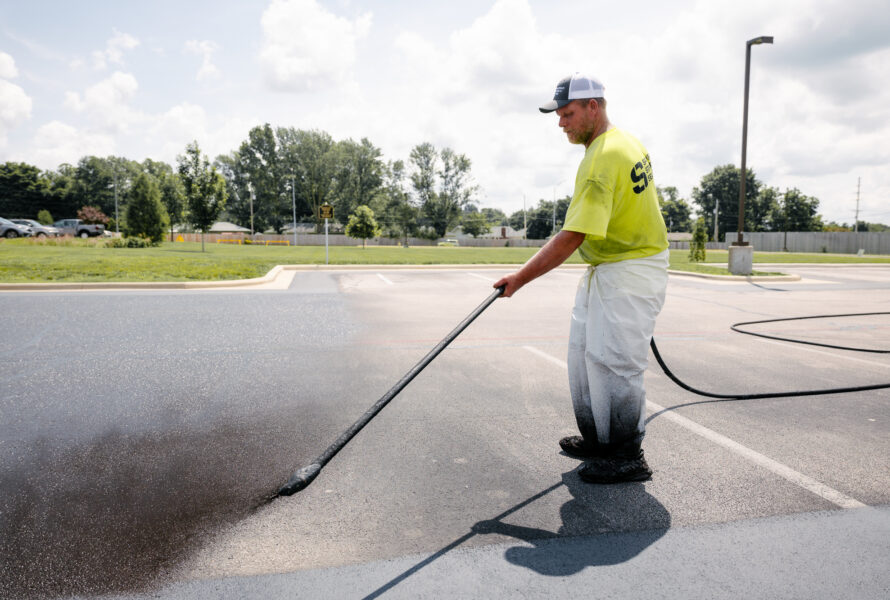 Worker sealing parking lot with long-handled sprayer.