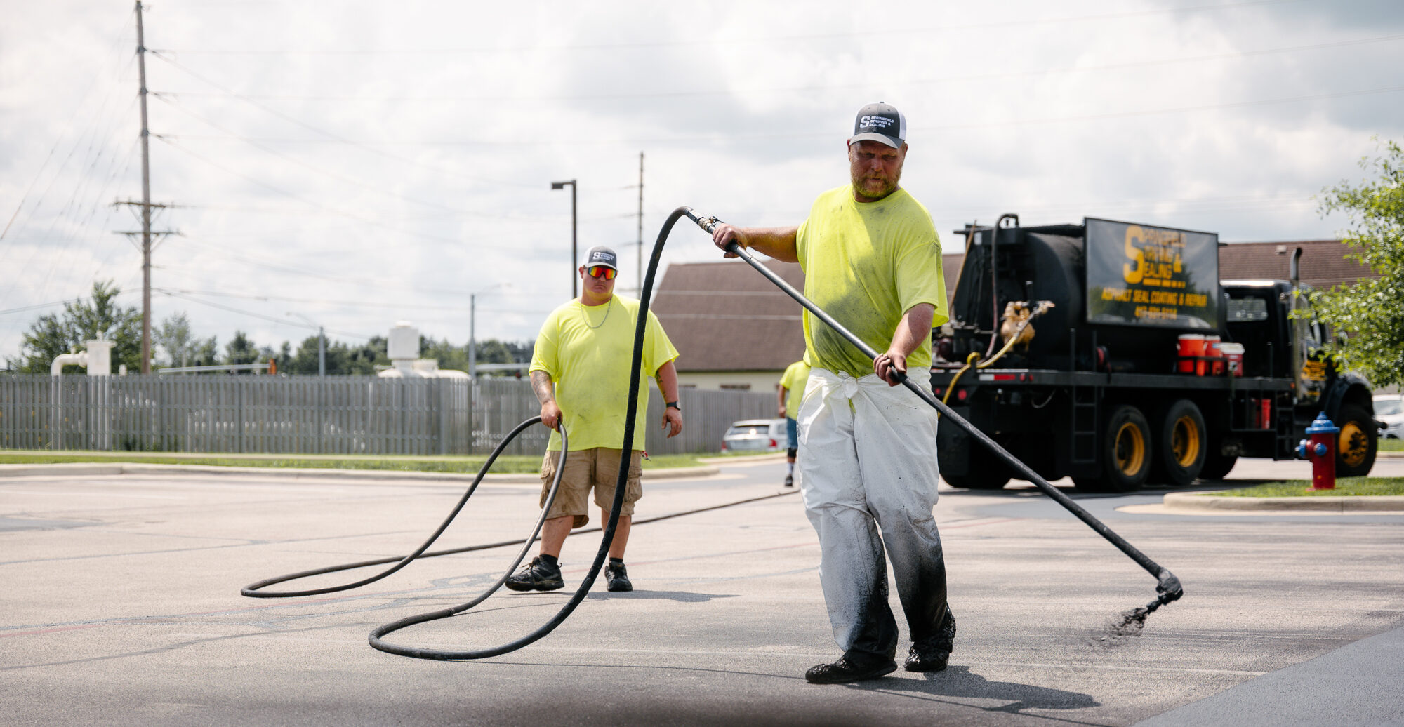 Worker sealing parking lot with long-handled sprayer.