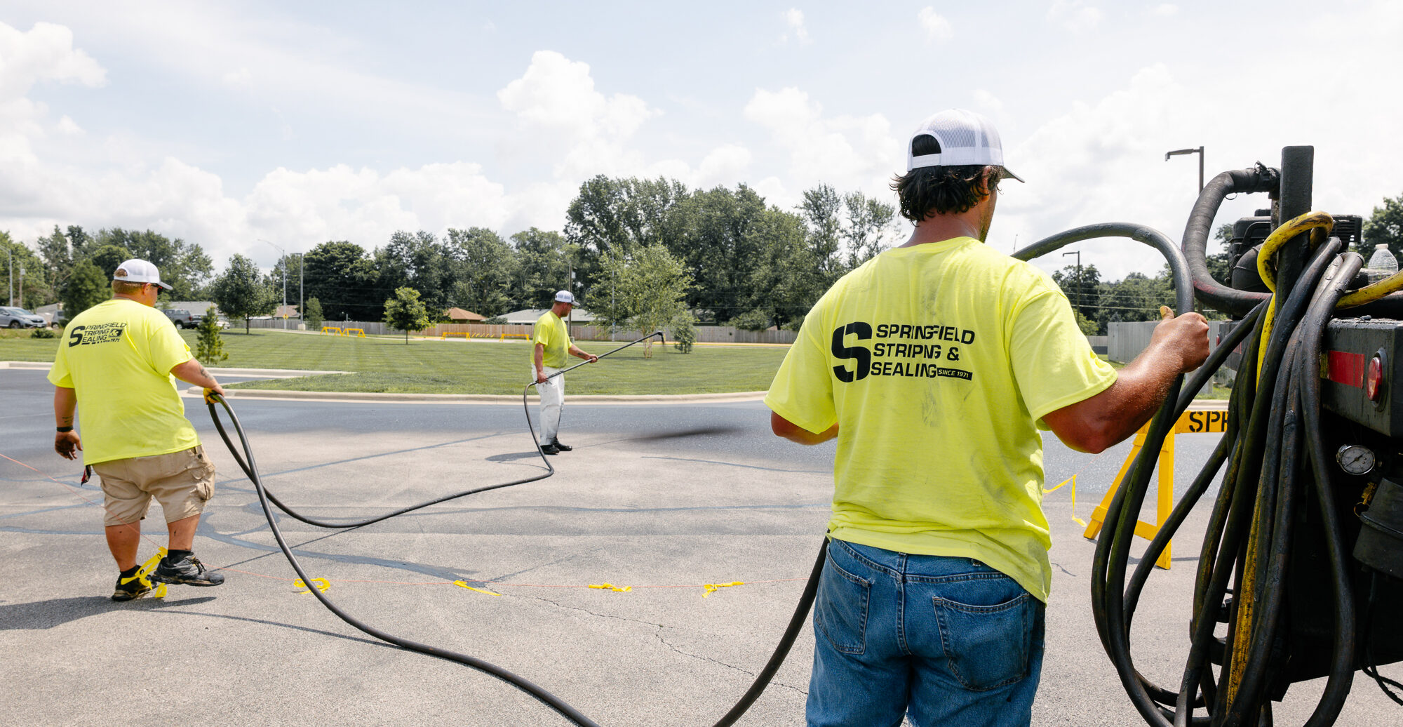 Worker sealing parking lot with long-handled sprayer.