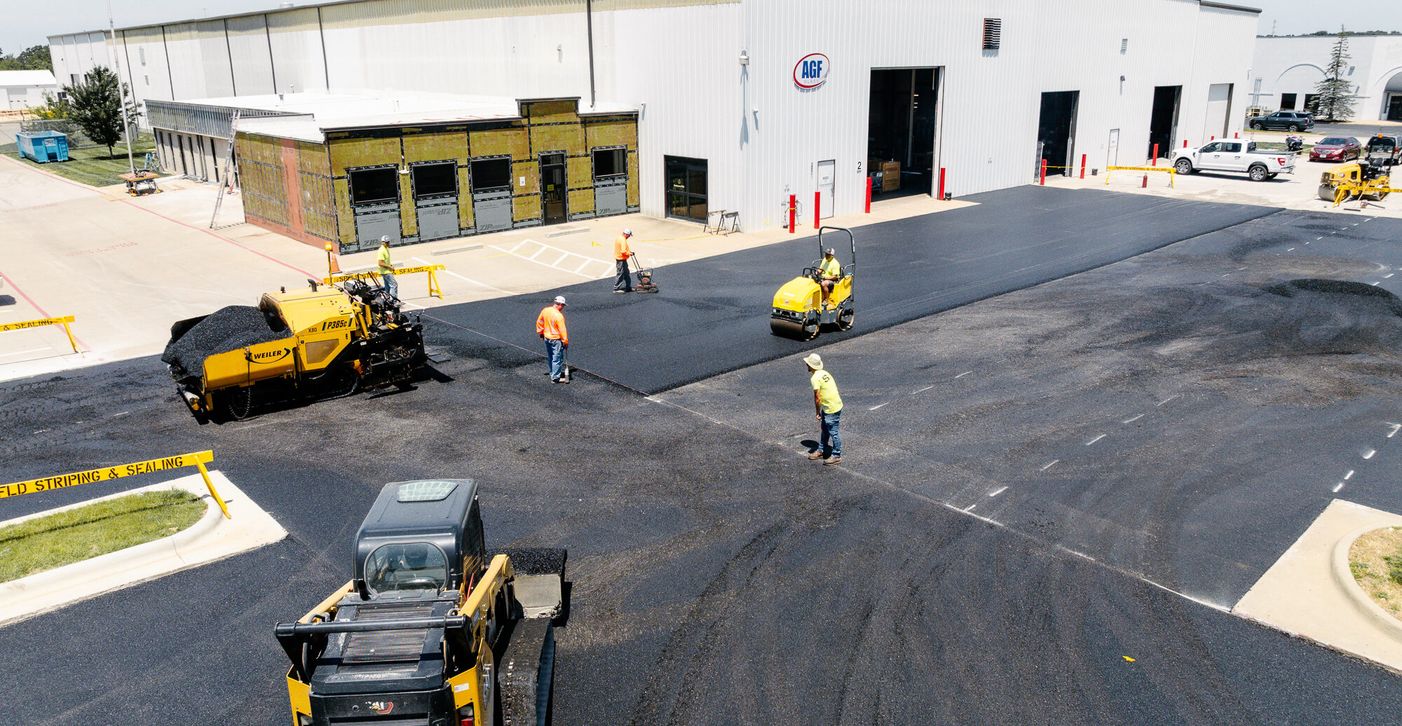 Workers pave parking lot in front of white AGF warehouse.