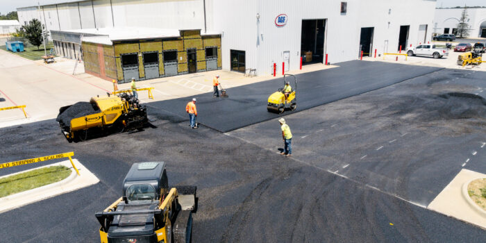Workers pave parking lot in front of white AGF warehouse.