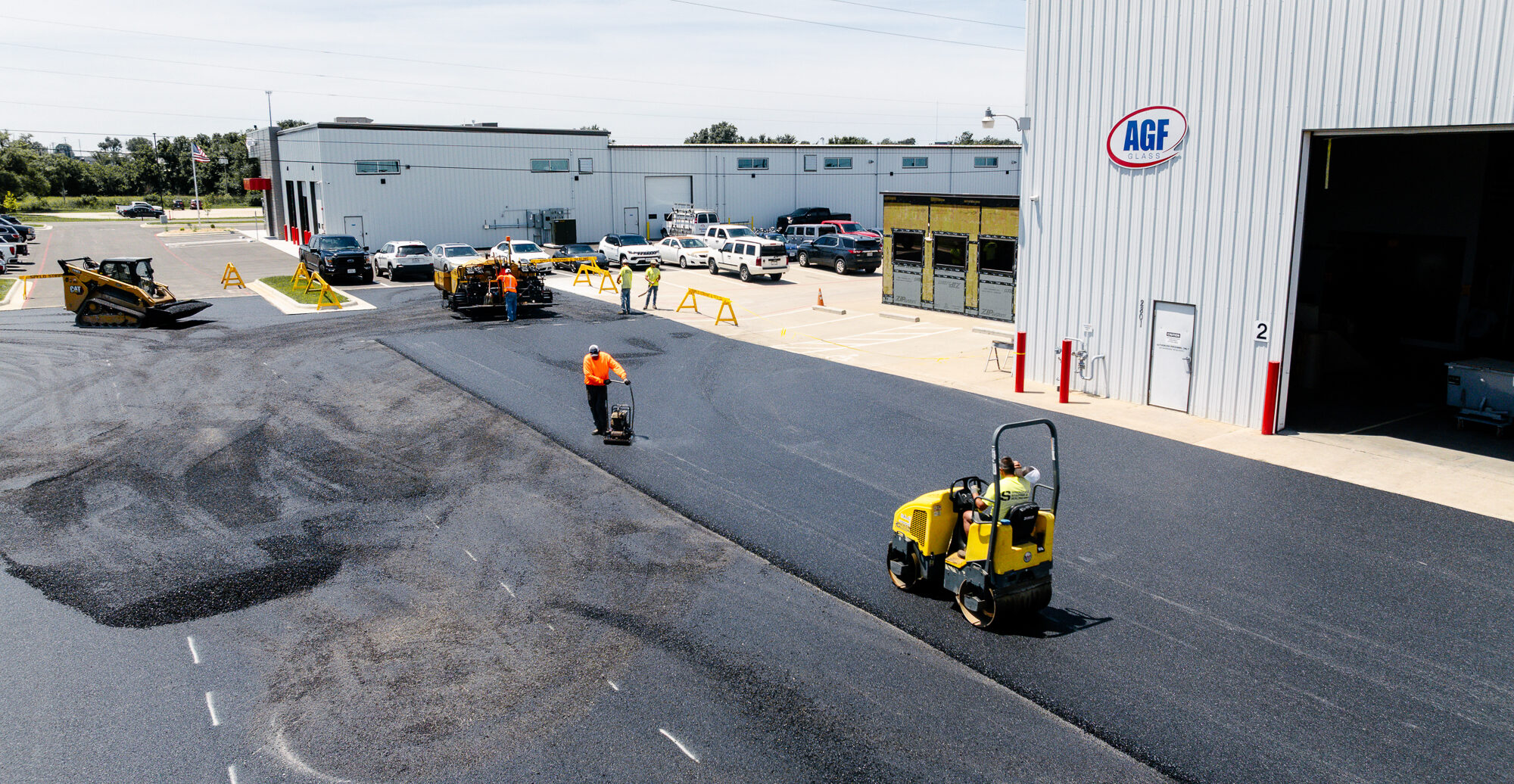 Workers pave parking lot in front of white AGF warehouse.