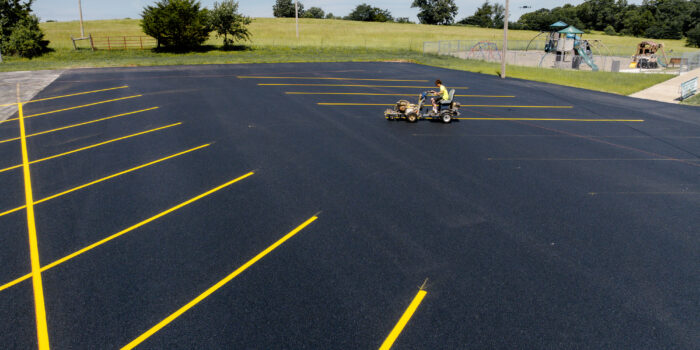 Worker painting yellow lines on new asphalt near playground.