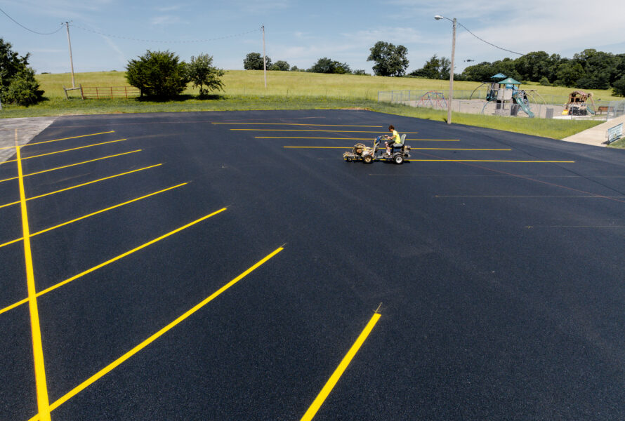 Worker painting yellow lines on new asphalt near playground.