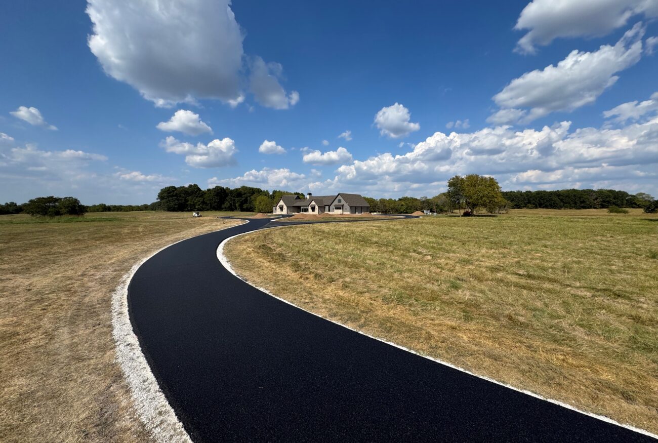 Curving asphalt path through grass leads to distant house.