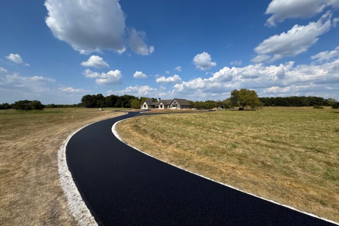Curving asphalt path through grass leads to distant house.