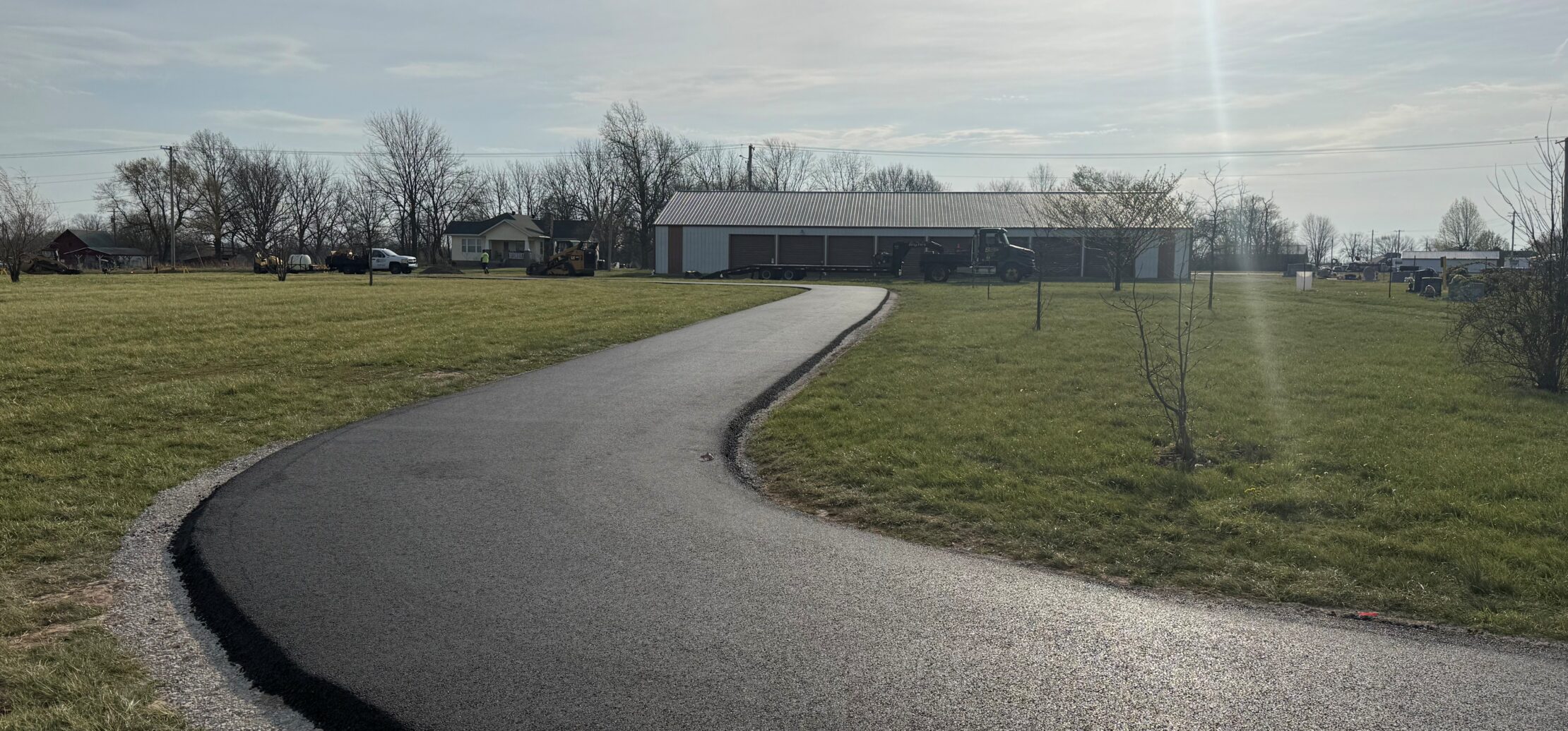 Workers paving asphalt road with nearby trucks and equipment.