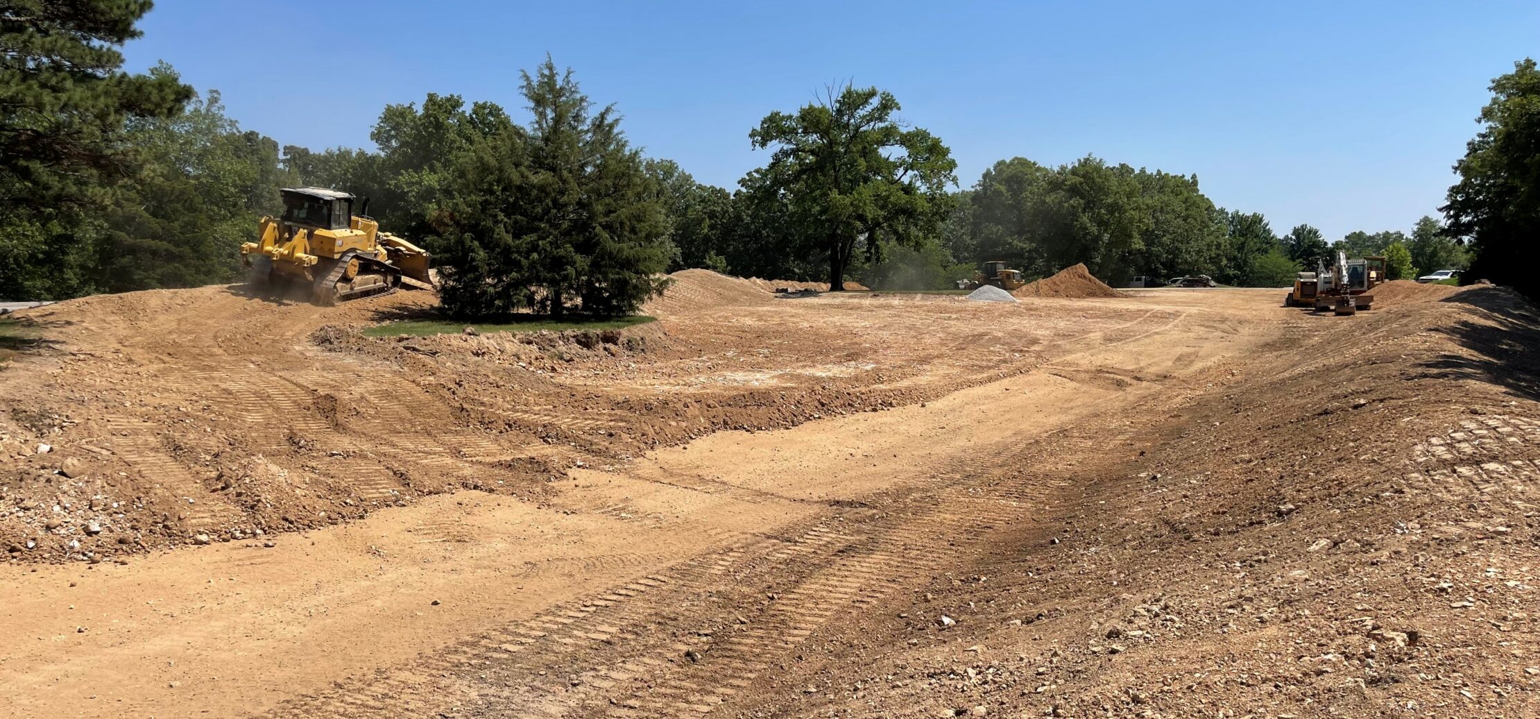 Workers pave new asphalt road with machinery, trees nearby.