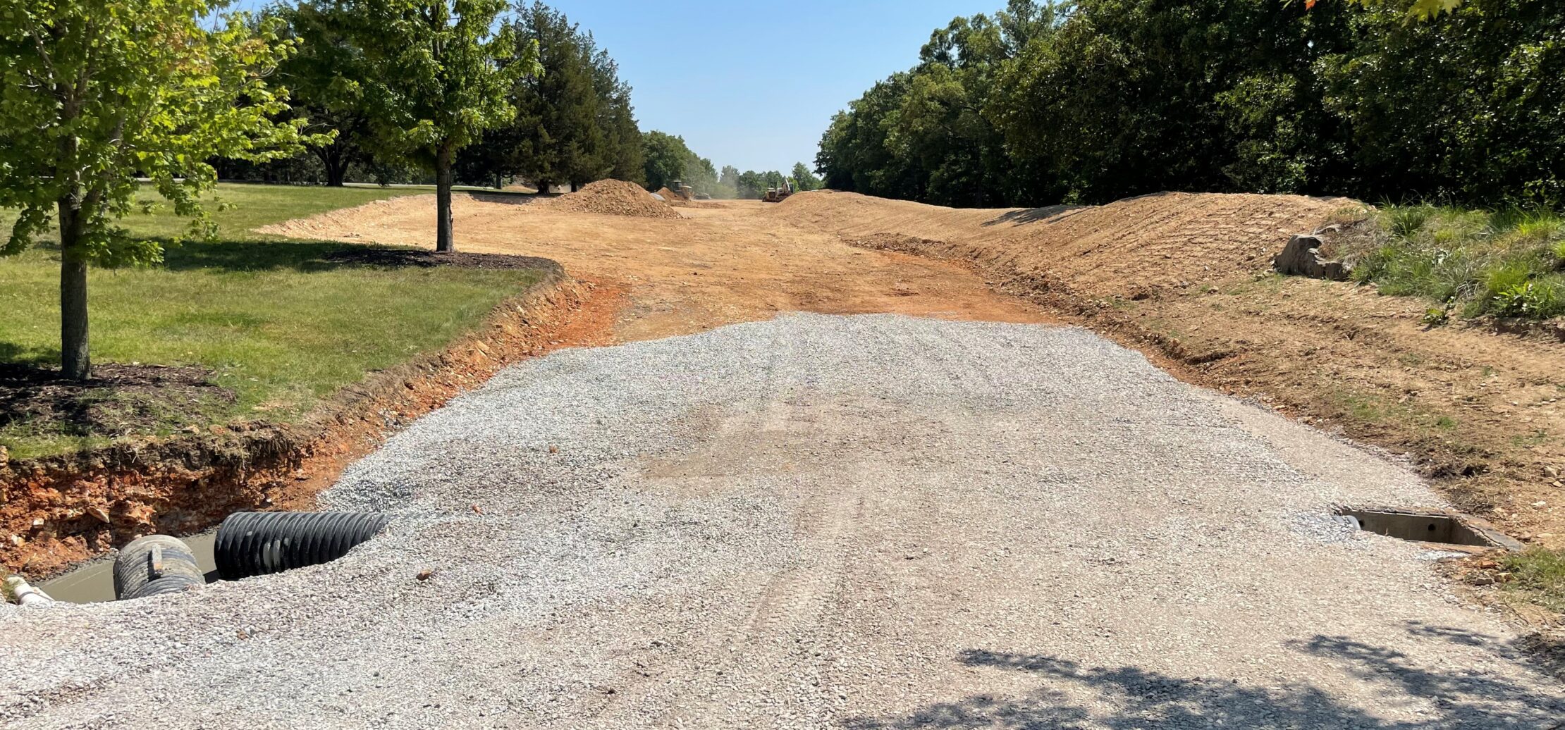 Workers pave new asphalt road with machinery, trees nearby.