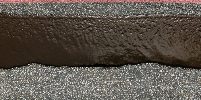 Red curb, black asphalt strip, and gravel pavement close-up.