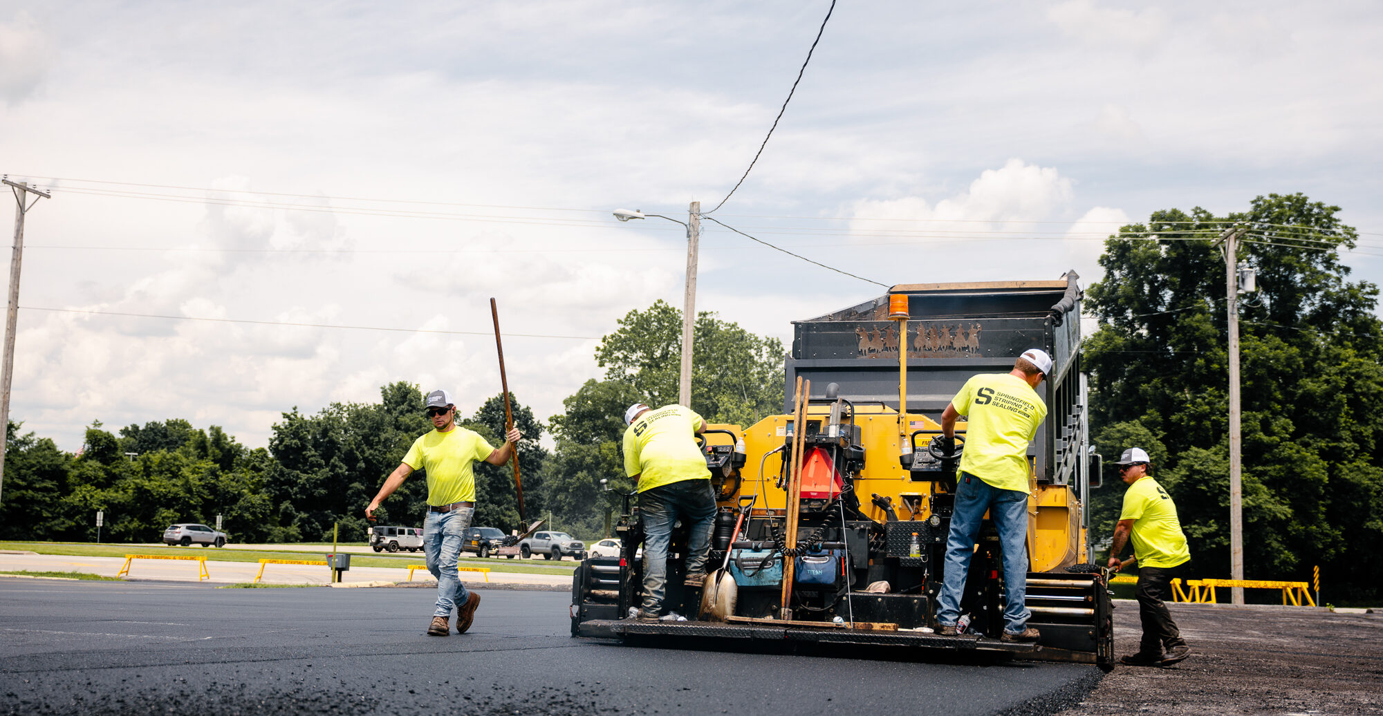 Worker in yellow spreading asphalt on parking lot.