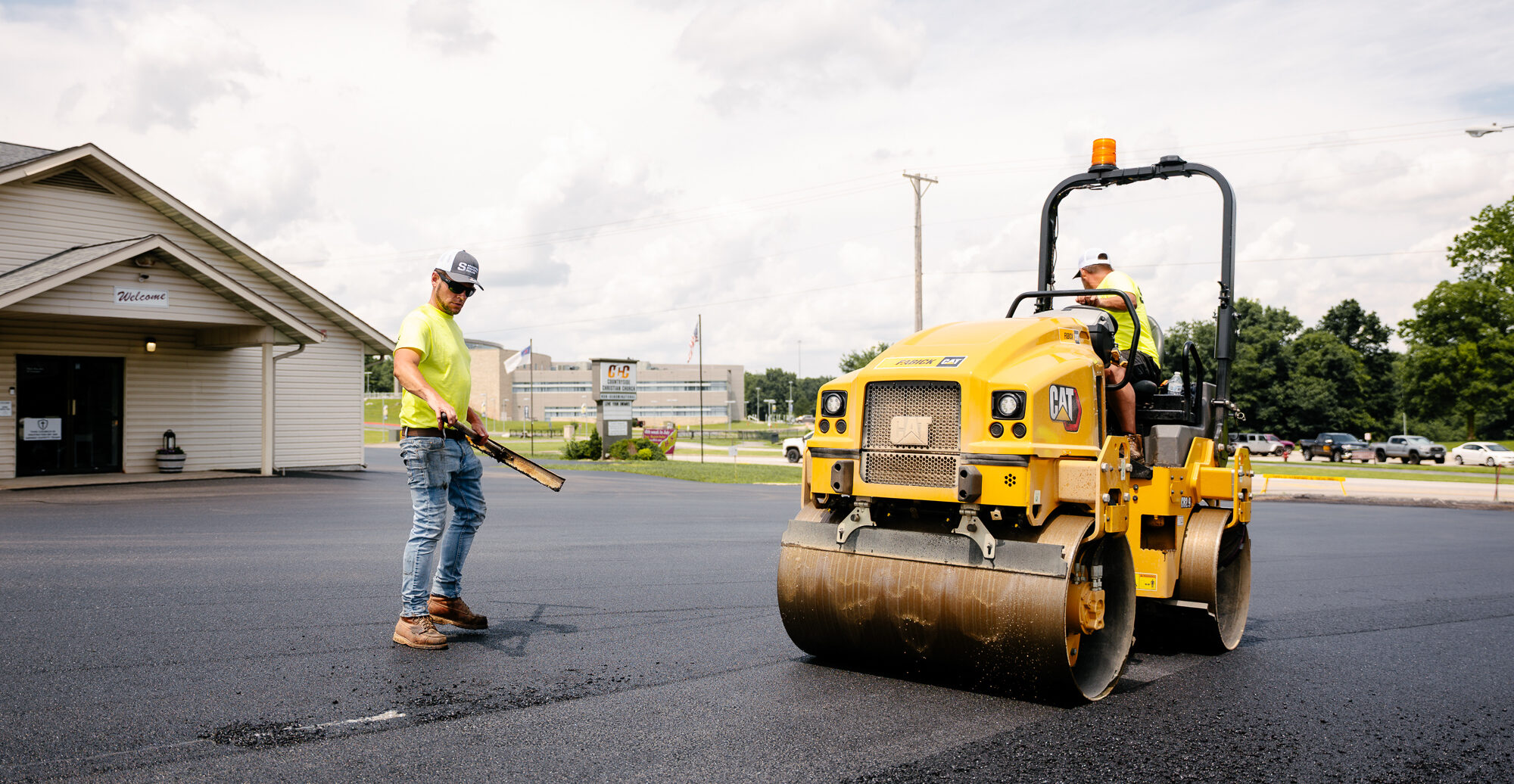 Worker in yellow spreading asphalt on parking lot.