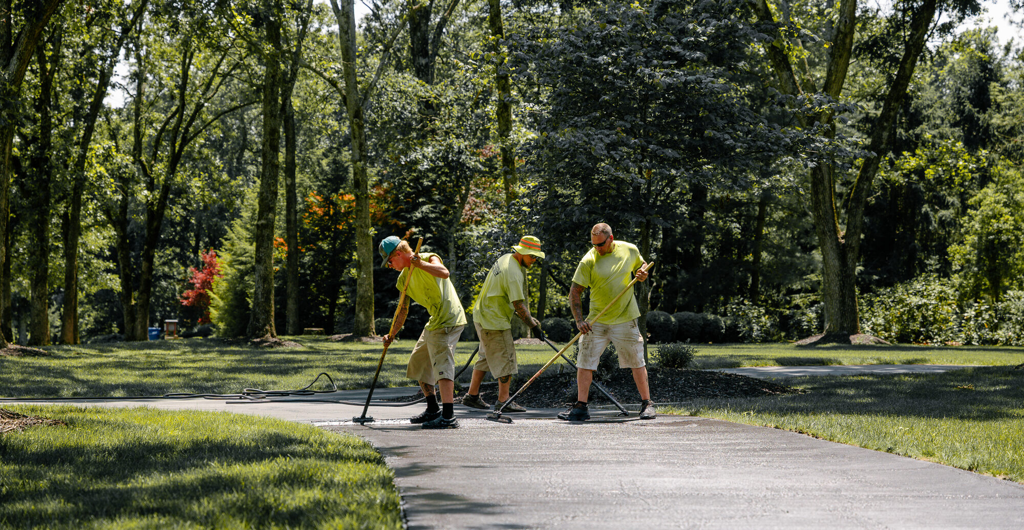 Workers with squeegees spread asphalt on a driveway.