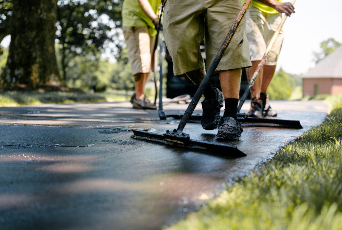 Workers with squeegees spread asphalt on a driveway.