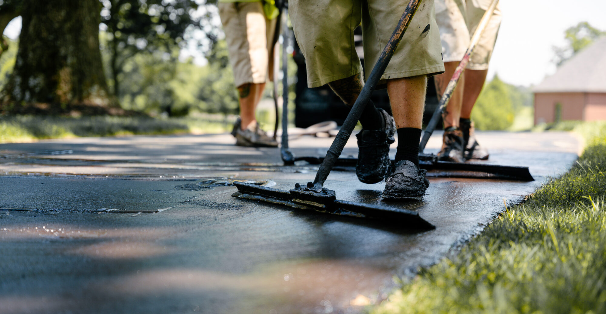 Workers with squeegees spread asphalt on a driveway.