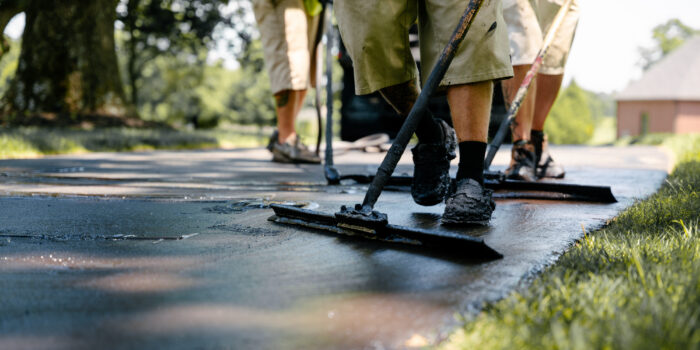 Workers with squeegees spread asphalt on a driveway.