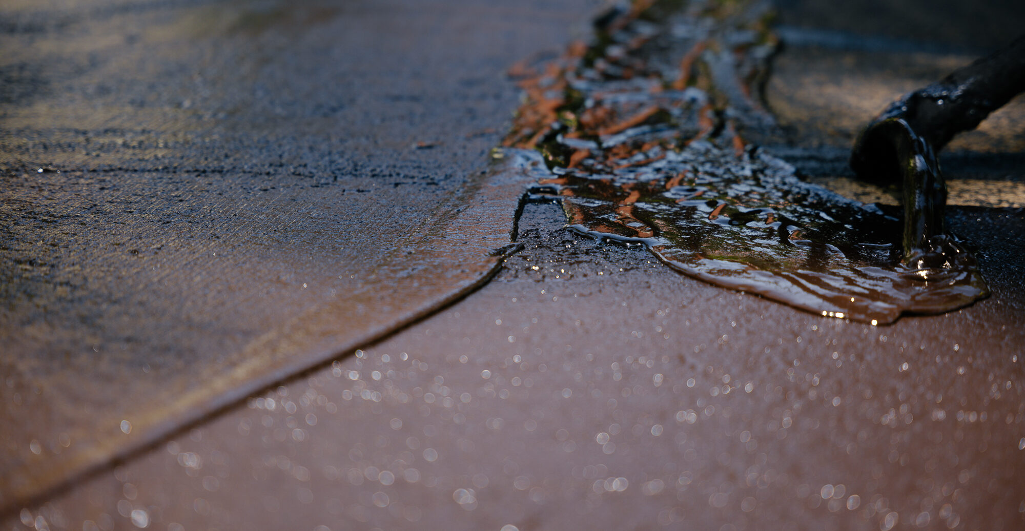 Workers with squeegees spread asphalt on a driveway.