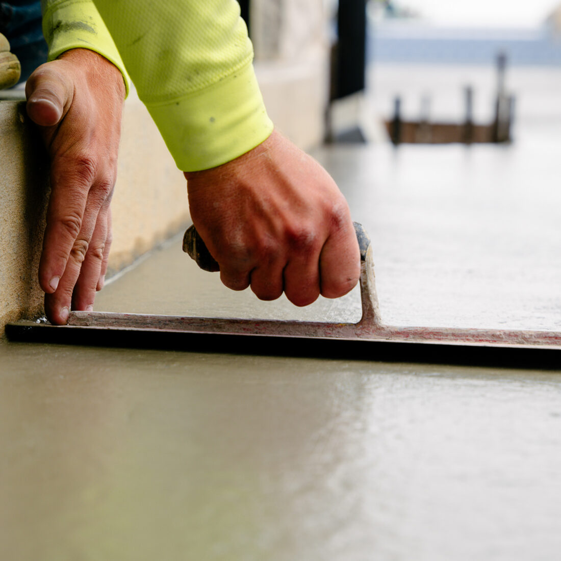 Person in yellow sleeve troweling wet concrete edge.