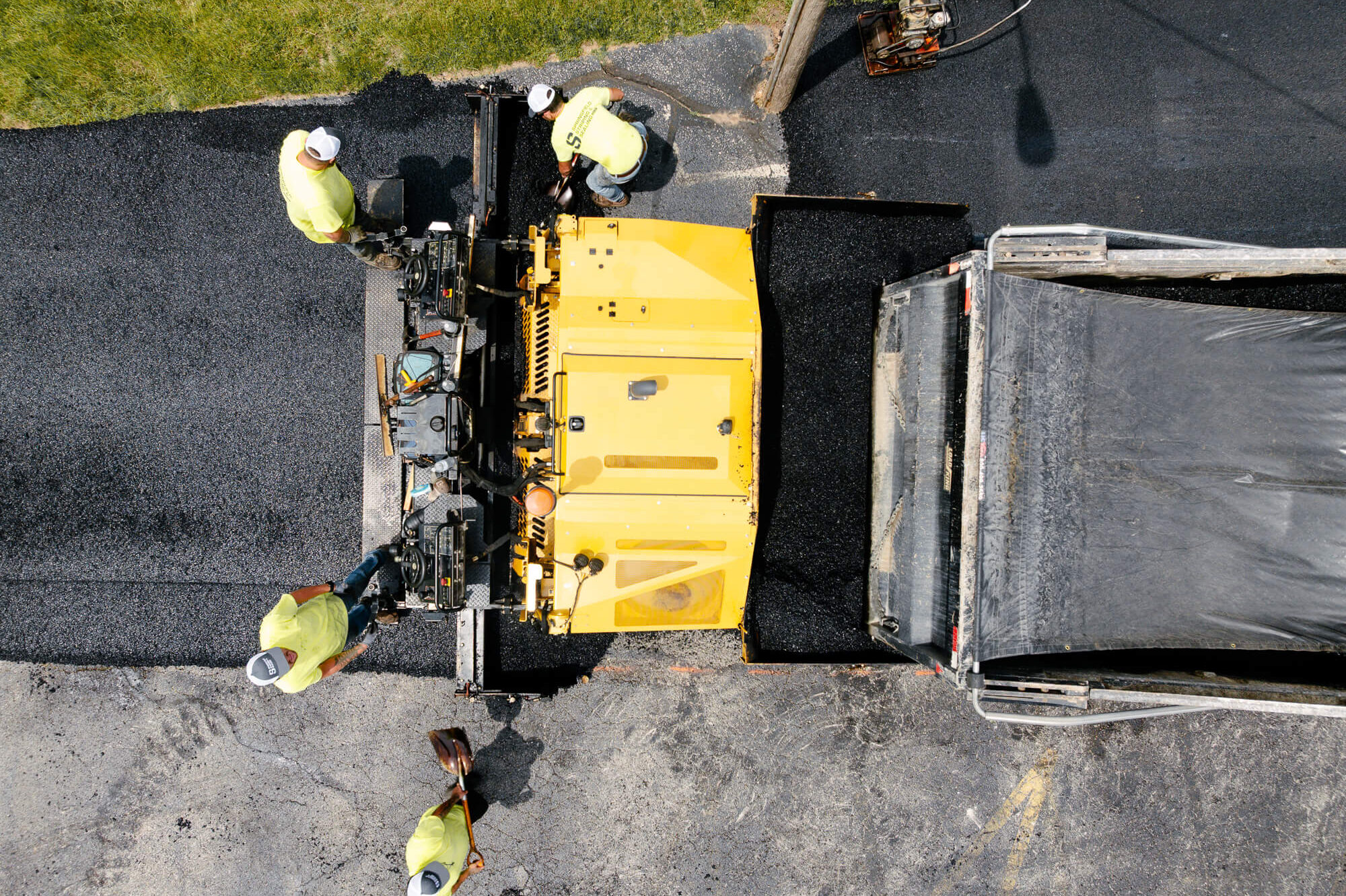 Workers paving road with yellow paver and dump truck.