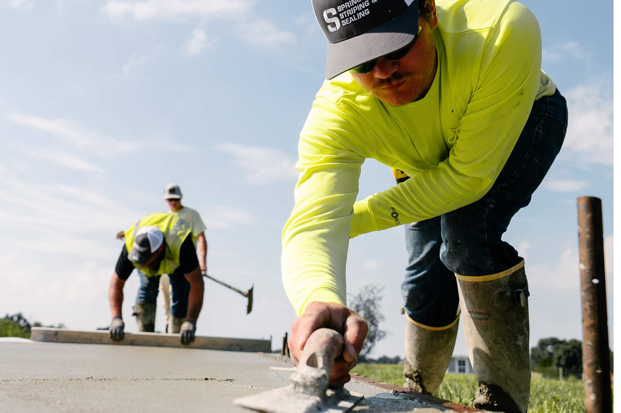 Workers in yellow shirts smooth concrete with trowels.