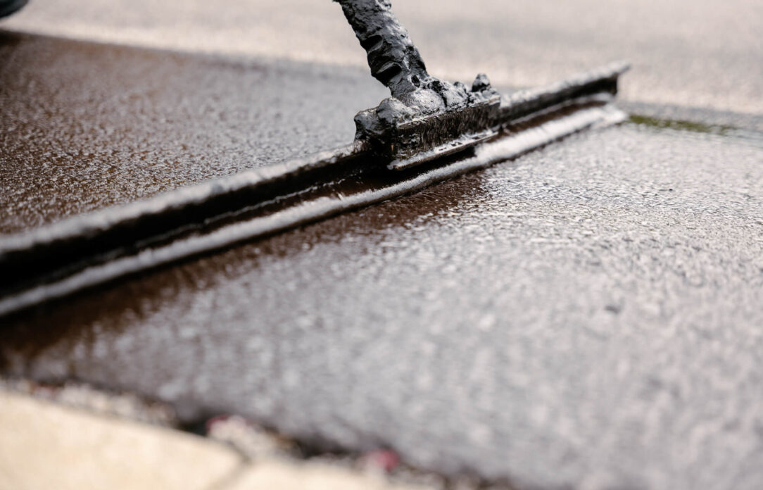 Tool spreading asphalt sealant on pavement, close-up view.