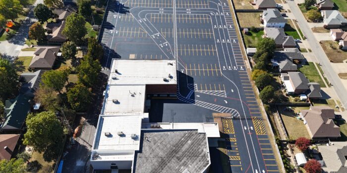 Aerial view of parking lot next to white-roofed building.