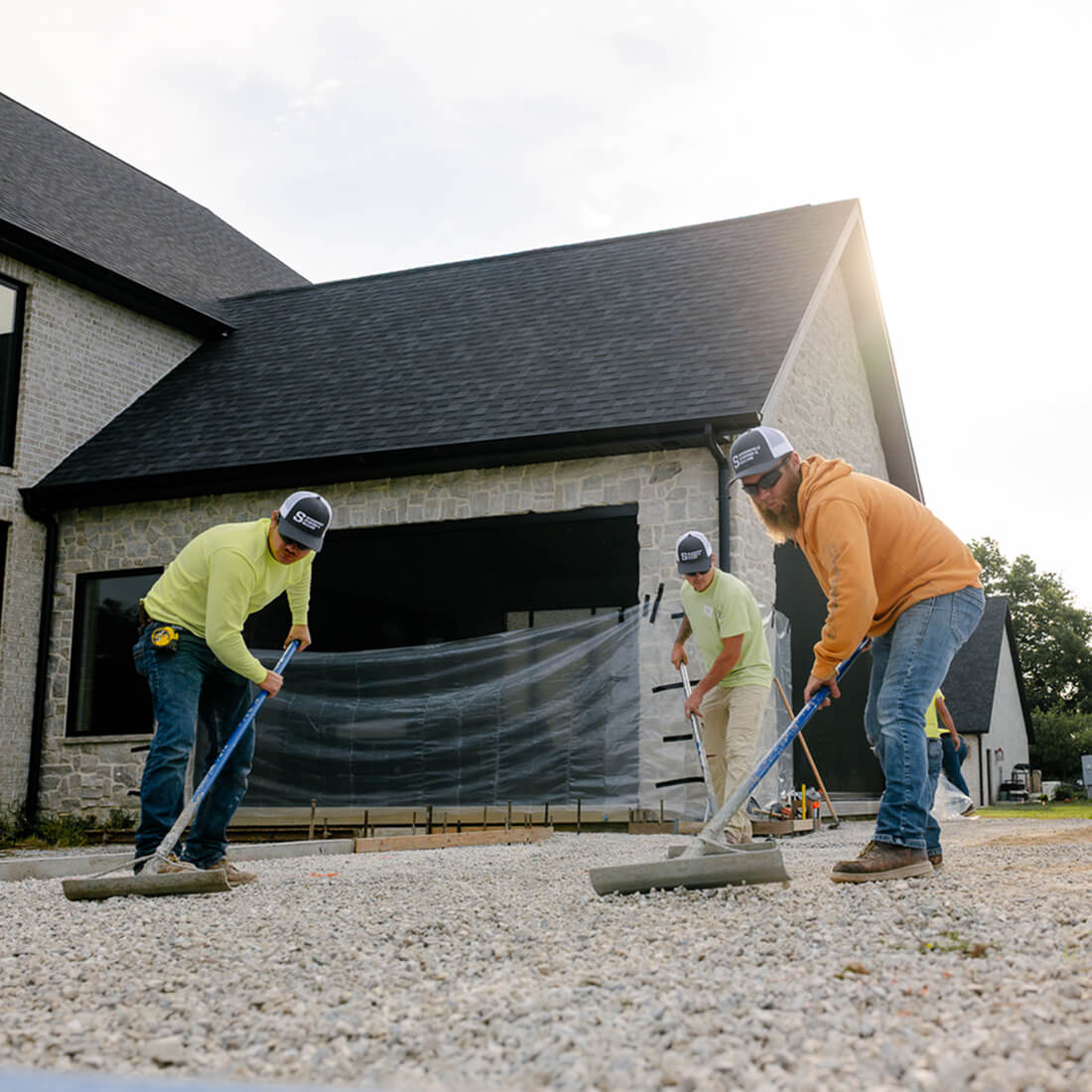 Workers level gravel before house with plastic-covered entry.