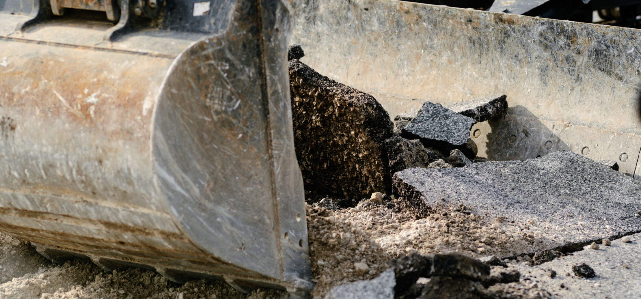 Two workers grade dirt with an excavator in the background.
