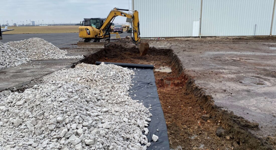 An excavator digging up a concrete parking lot.