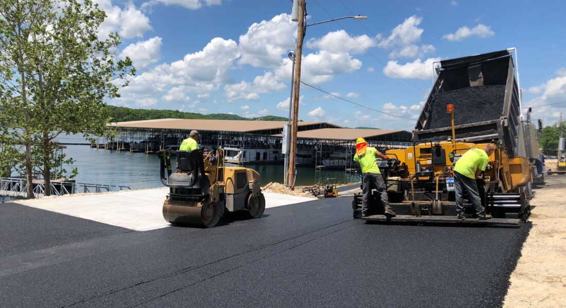 Team of workers pave a road next to a lake.