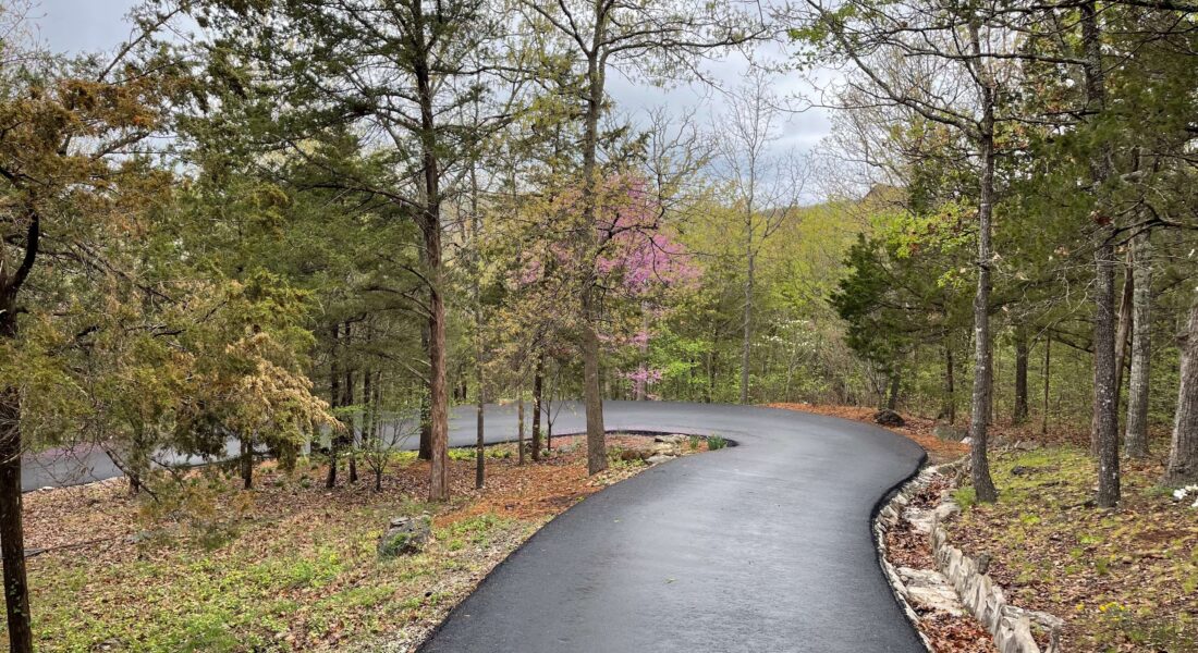 A new asphalt driveway surrounded by trees.