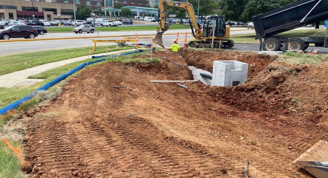Equipment excavating land next to a busy street.
