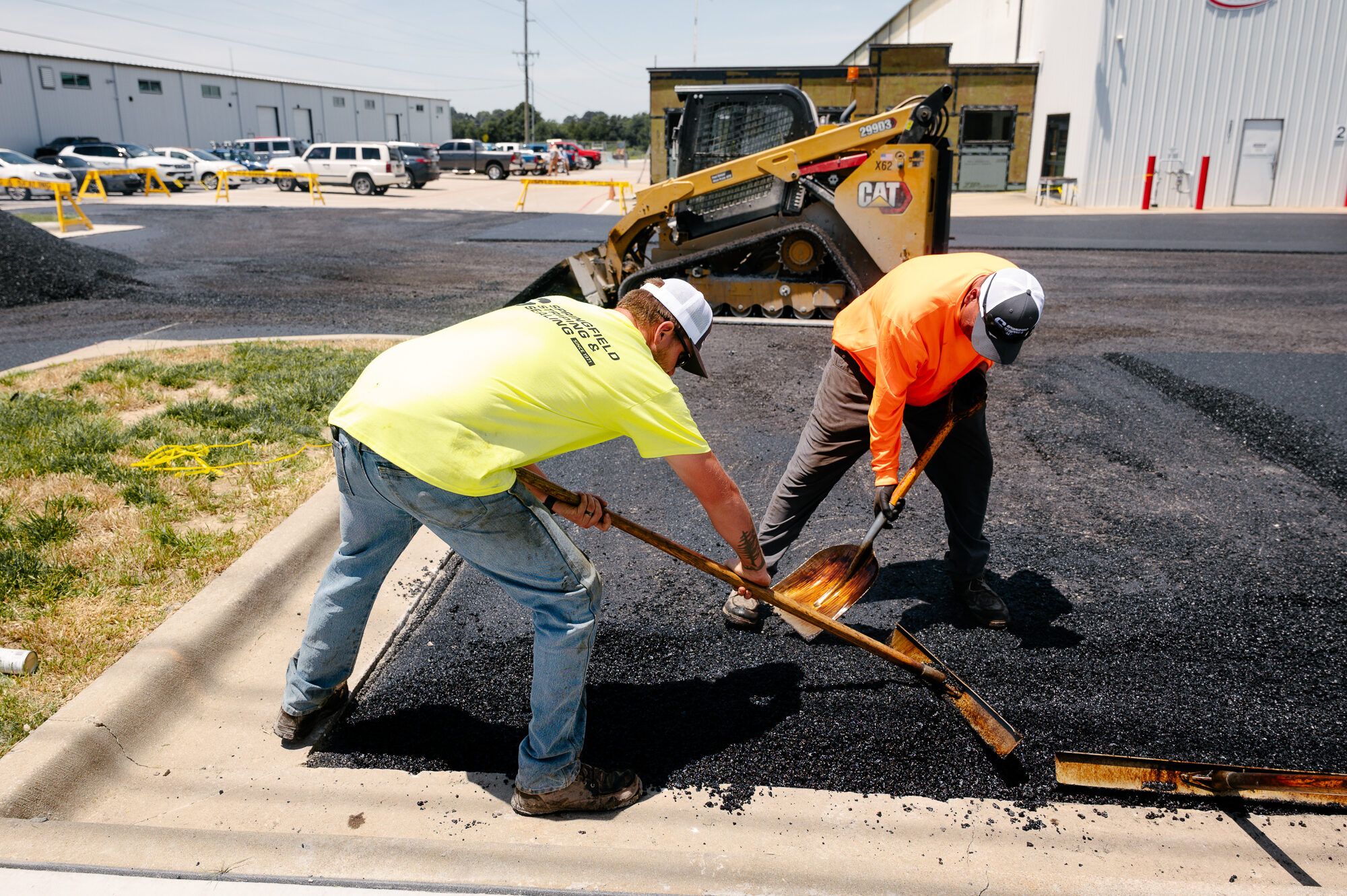 Workers smooth new asphalt near skid steer loader.