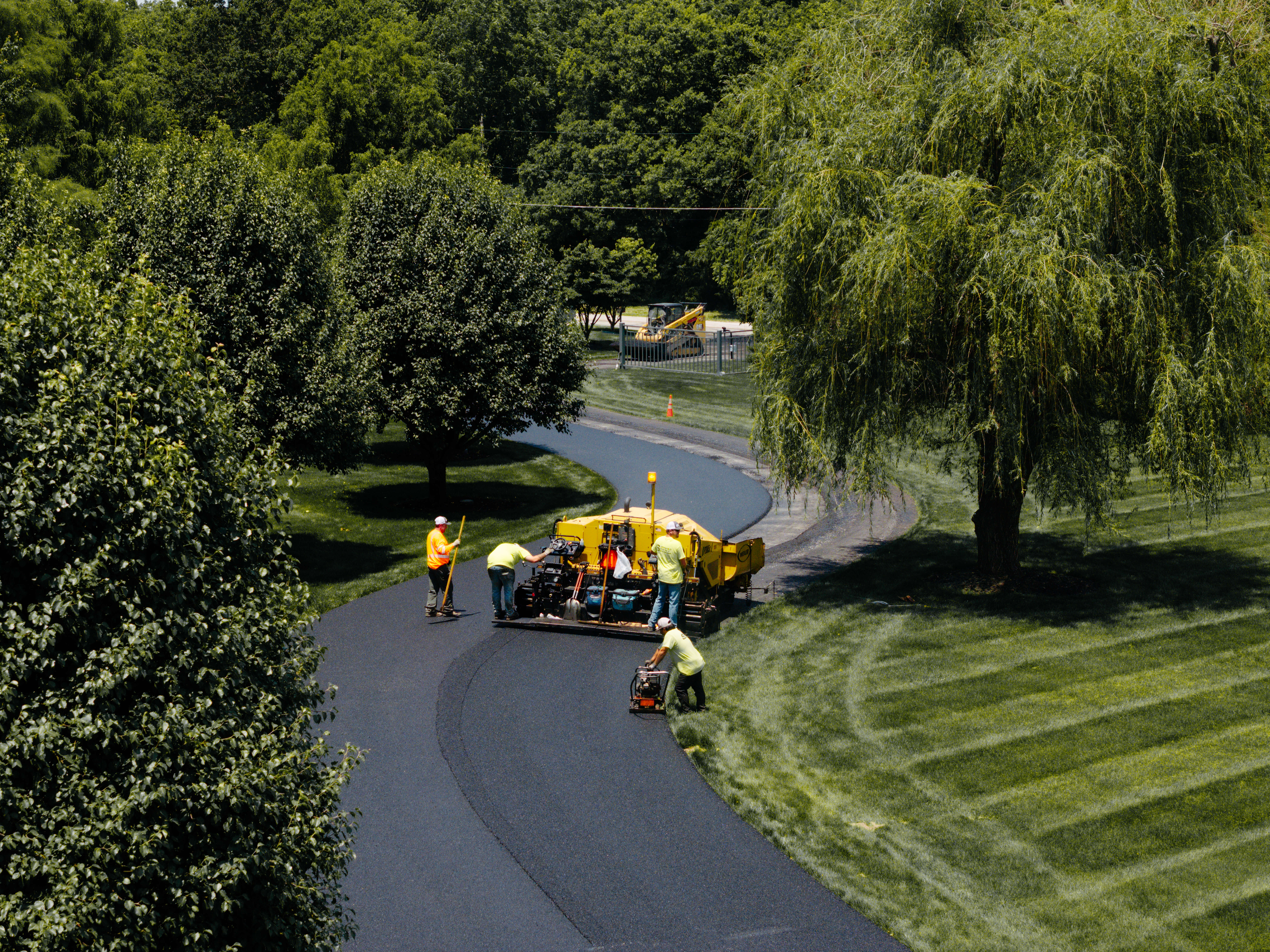 A team paves a road surrounded by greenery.