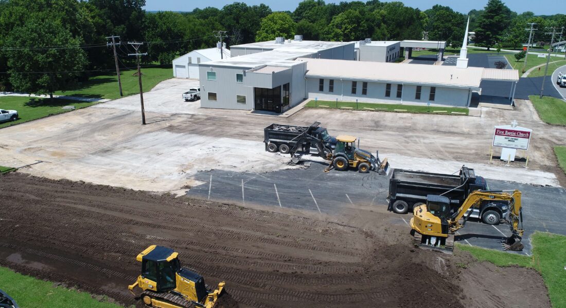 Overhead shot of yellow equipment excavating a parking lot.