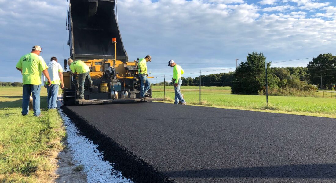 Team of workers lay hot asphalt.