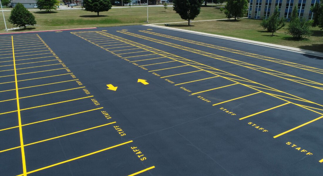 A freshly paved parking lot with yellow staff parking spots and directional arrows.