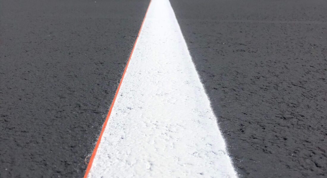 Photo of a white line in a parking lot with trees and a blue sky in the background.