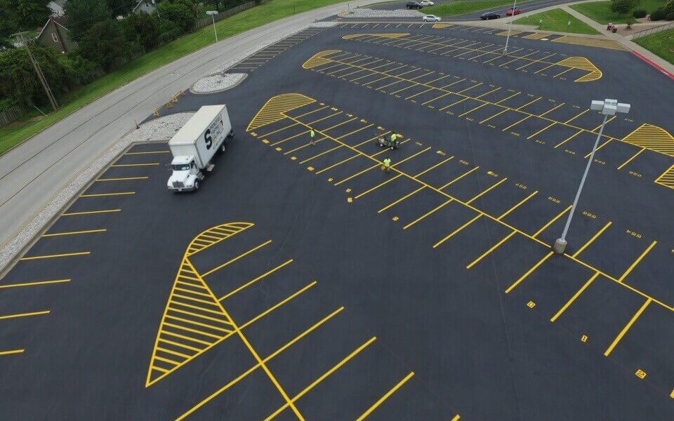 A birds eye view of workers finishing up on a newly paved and striped parking lot.