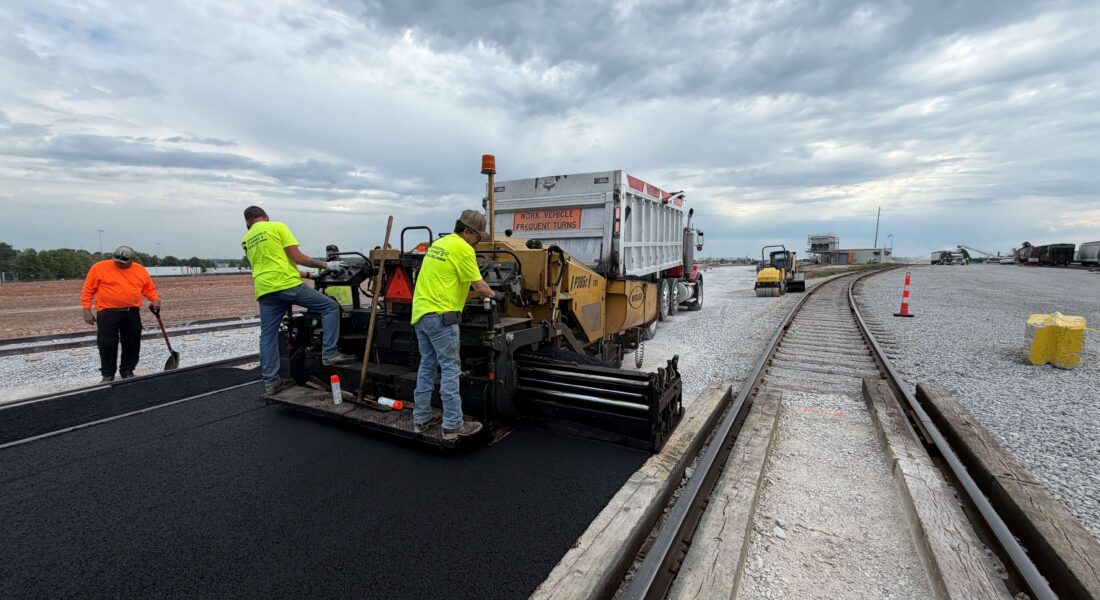 Team of workers lays asphalt next to a railroad.