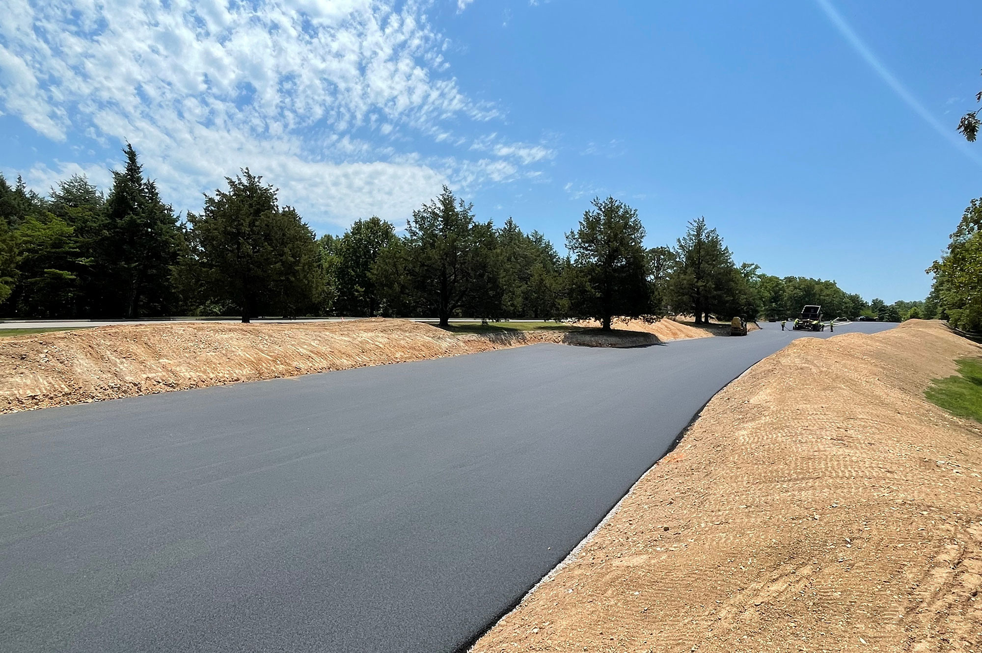 Asphalt road flanked by dirt embankments and trees.