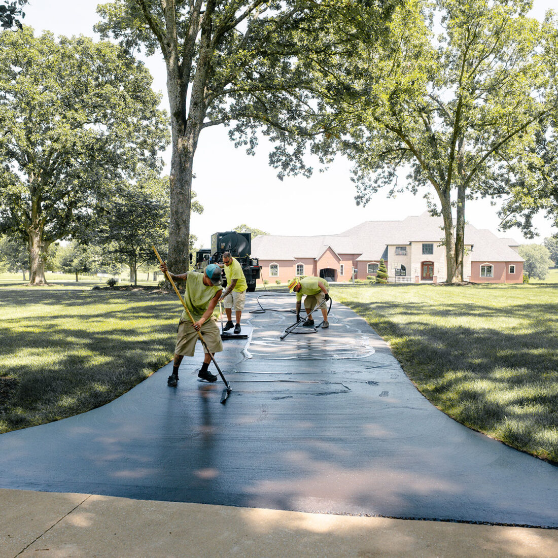 Three workers coat a driveway to a house.