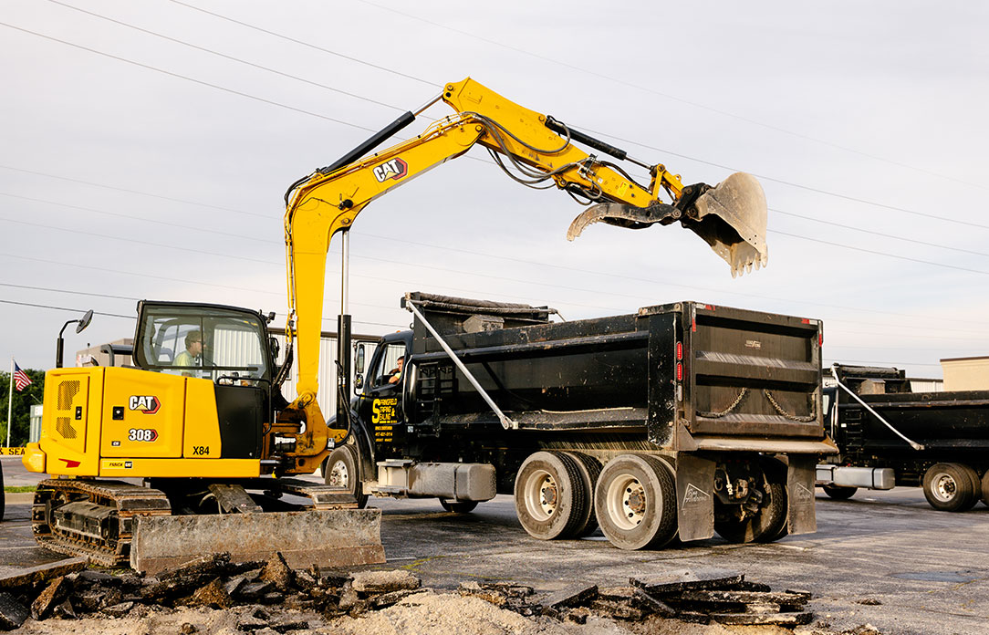 Yellow excavator loads debris into black dump truck nearby.