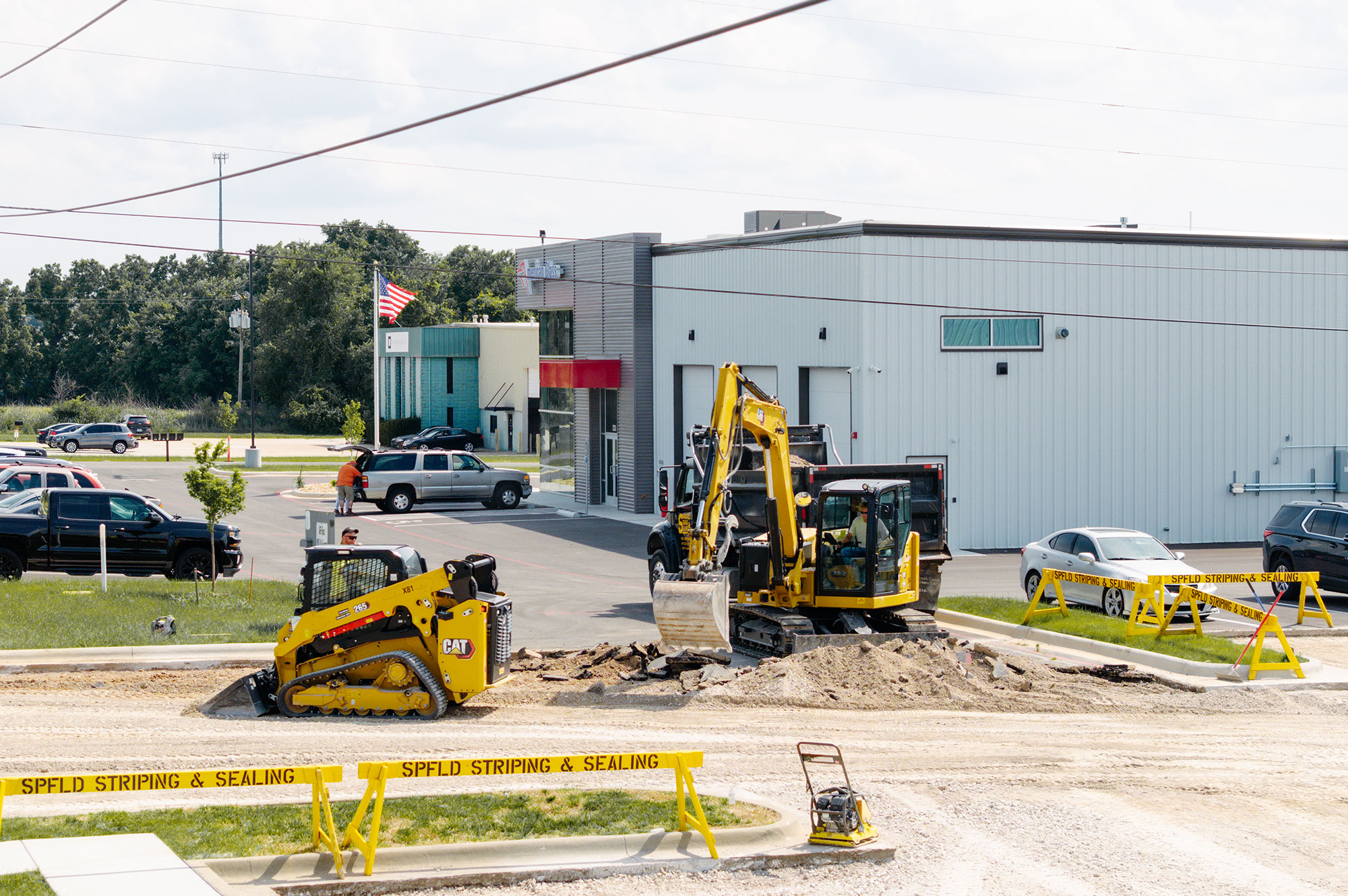 Construction vehicles operate on a dug-up road near buildings.