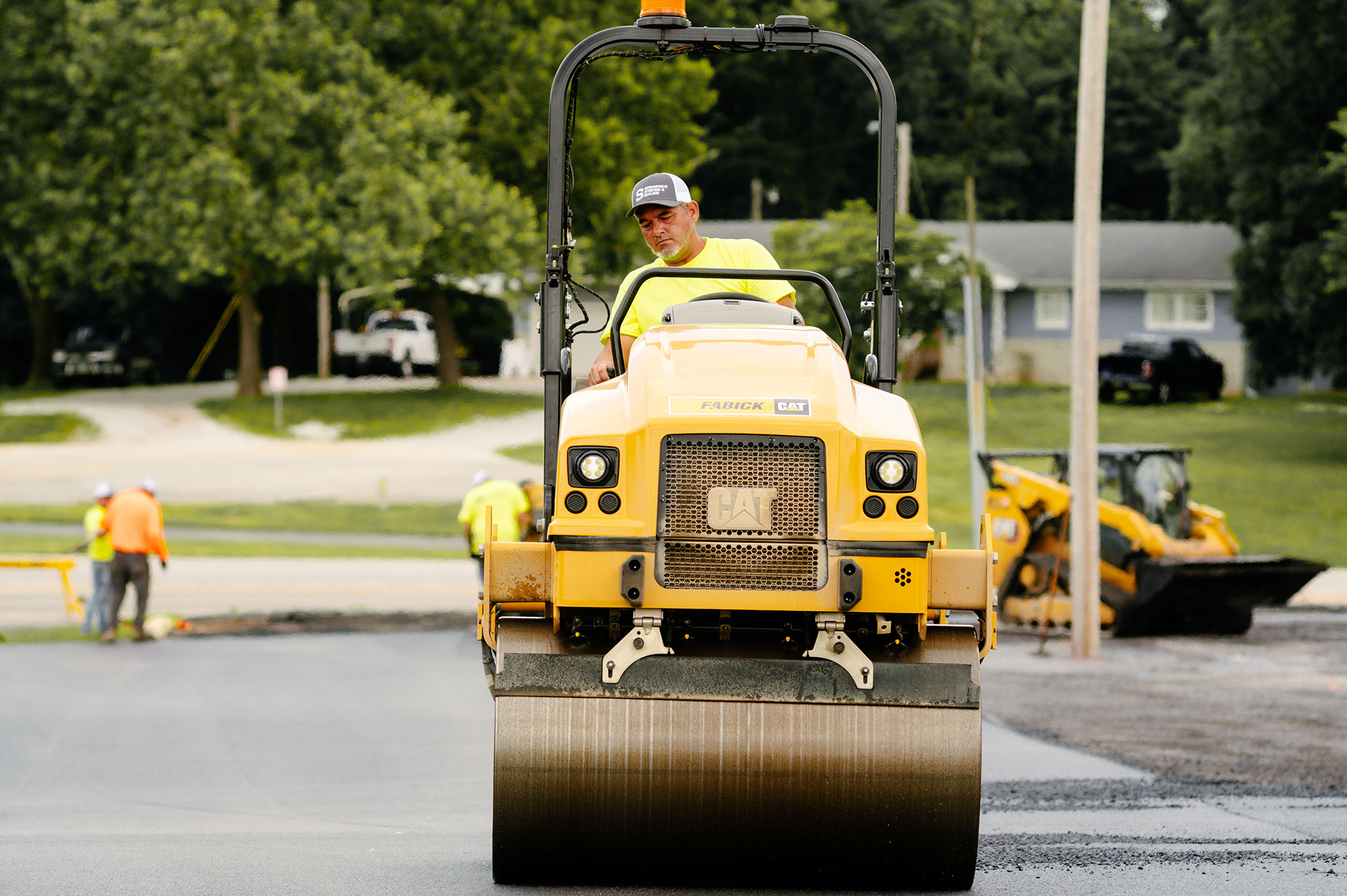 Worker drives yellow CAT road roller on new asphalt.